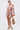Woman wearing the CRAZY IN LOVE SATIN ROMPER—an orange and white patterned satin romper with a deep V-neck, flowy silhouette, and cutout waist—styled with hoop earrings, silver heels, and a woven straw bag against a white background.