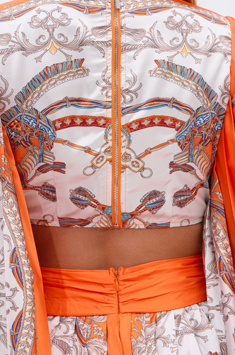 A close-up of a person wearing the CRAZY IN LOVE SATIN ROMPER featuring a colorful baroque scarf print, orange waistband, intricate blue, orange, and white designs, and a visible back zipper that highlights its flowy silhouette.