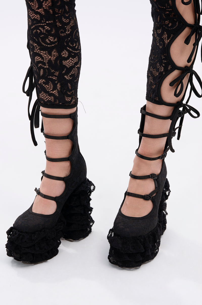 Person wearing black lace-up leggings and AZALEA WANG SPREENE FRILL LACE PUMP IN BLACK, featuring layered ruffle details and multiple straps, standing on a white background.