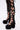 Close-up of a person wearing black lace-up leggings with cutouts and the AZALEA WANG SPREENE FRILL LACE PUMP IN BLACK—gothic platform shoes with chunky heels, multiple straps, and ruffled lace. Set against a plain white background.