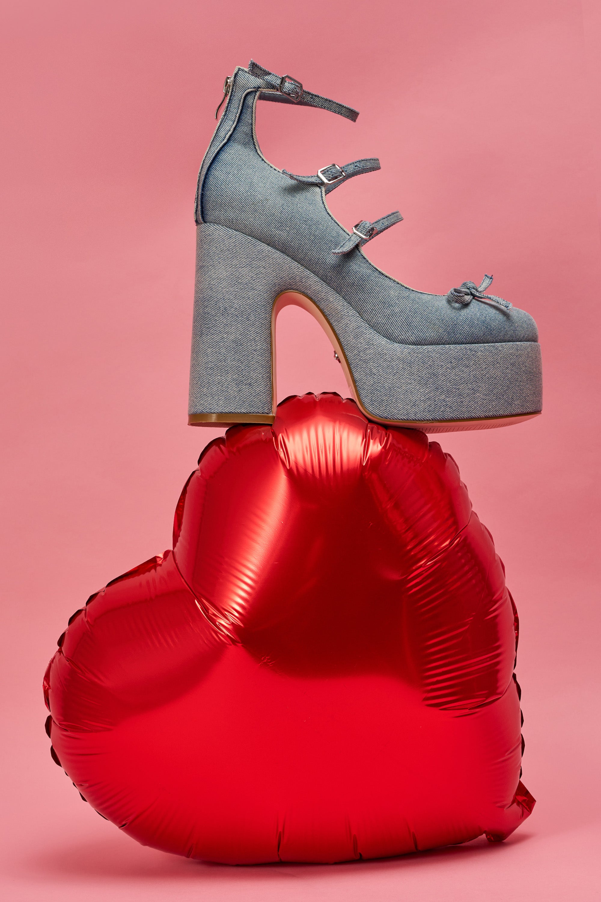 The AZALEA WANG SPROUT DENIM CHUNKY PUMP, featuring a comfort cushion insole and ankle straps, is displayed atop a shiny red heart-shaped balloon set against a pink background. 1