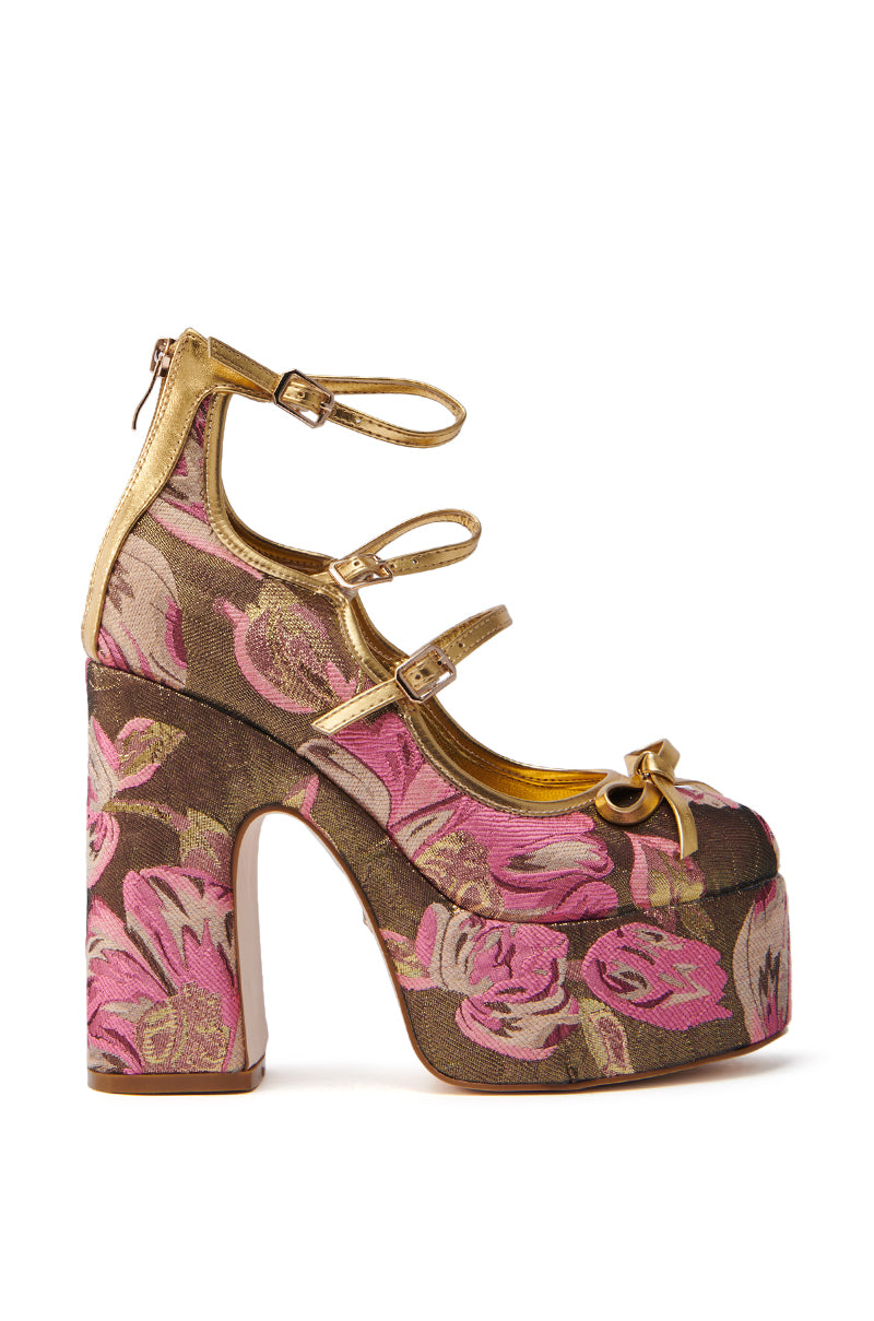 The AZALEA WANG SPROUT GOLD BROCADE PUMP is a high platform shoe with a pink and gold floral pattern. It features two ankle straps, an open-toe design with bow detailing, and a mega-chunky heel adorned with a flower print for an elegant standout look.