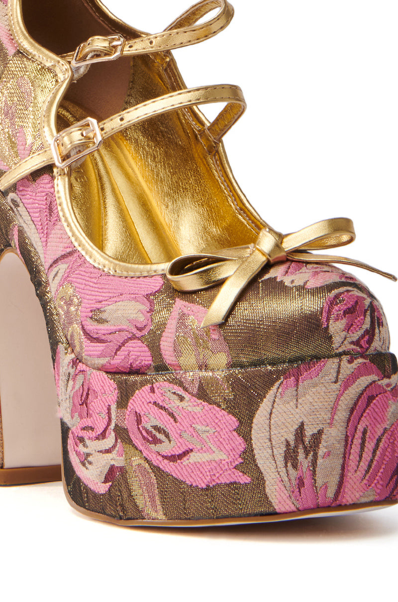 A close-up view of the AZALEA WANG SPROUT GOLD BROCADE PUMP showcases its vibrant platform sole, adorned with pink and purple floral details. Gold metallic straps and a decorative bow embellish the front, while an opulent gold lining completes this chic accessory.