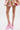A person stands against a white background wearing a pink and gold patterned skirt and the AZALEA WANG SPROUT PINK CHUNKY PUMP, featuring light pink floral lace platform heels with ankle straps.