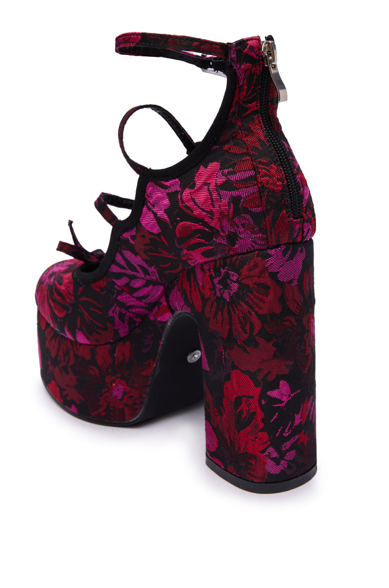 The AZALEA WANG SPROUT Red Multi Floral Brocade Mary Jane Platform Pump features a bold red and pink floral pattern, chunky heel, multiple black straps, and an ankle zipper.