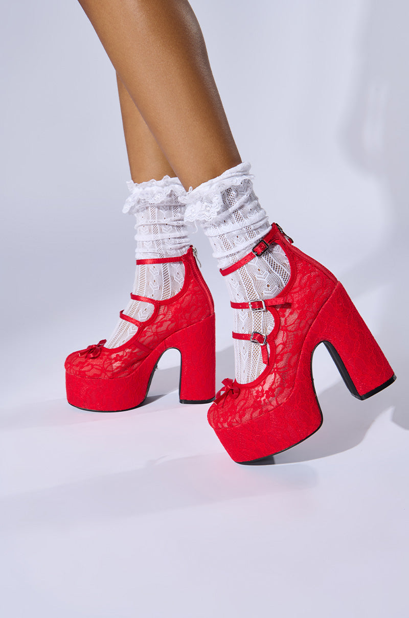 A person wearing white lace socks and the AZALEA WANG SPROUT RED PUMPs with multiple straps stands against a white background. The shoes have a floral lace texture and chunky high heels.