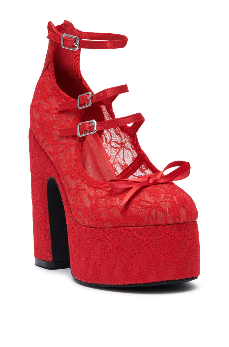 The AZALEA WANG SPROUT RED PUMP showcases a vibrant red platform heel adorned with intricate lace. It features multiple straps with petite buckles, accented by a decorative bow at the toe. The shoe is designed with a chunky heel and a high arch, delivering an audacious and chic aesthetic.