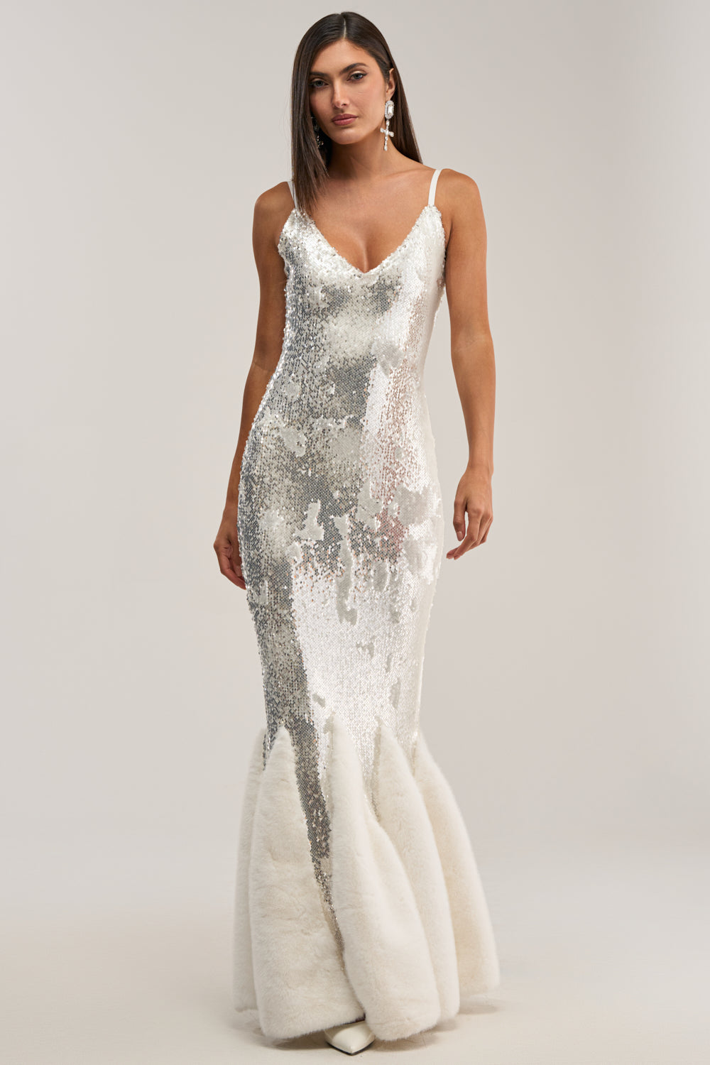 A woman in the WORTH THE STARES EMBELLISHED MAXI DRESS—white, sequin mermaid style with thin straps and a fitted bodice, flaring into fluffy fabric—stands against a plain background. Ideal for formal events, her straight brown hair completes the look.