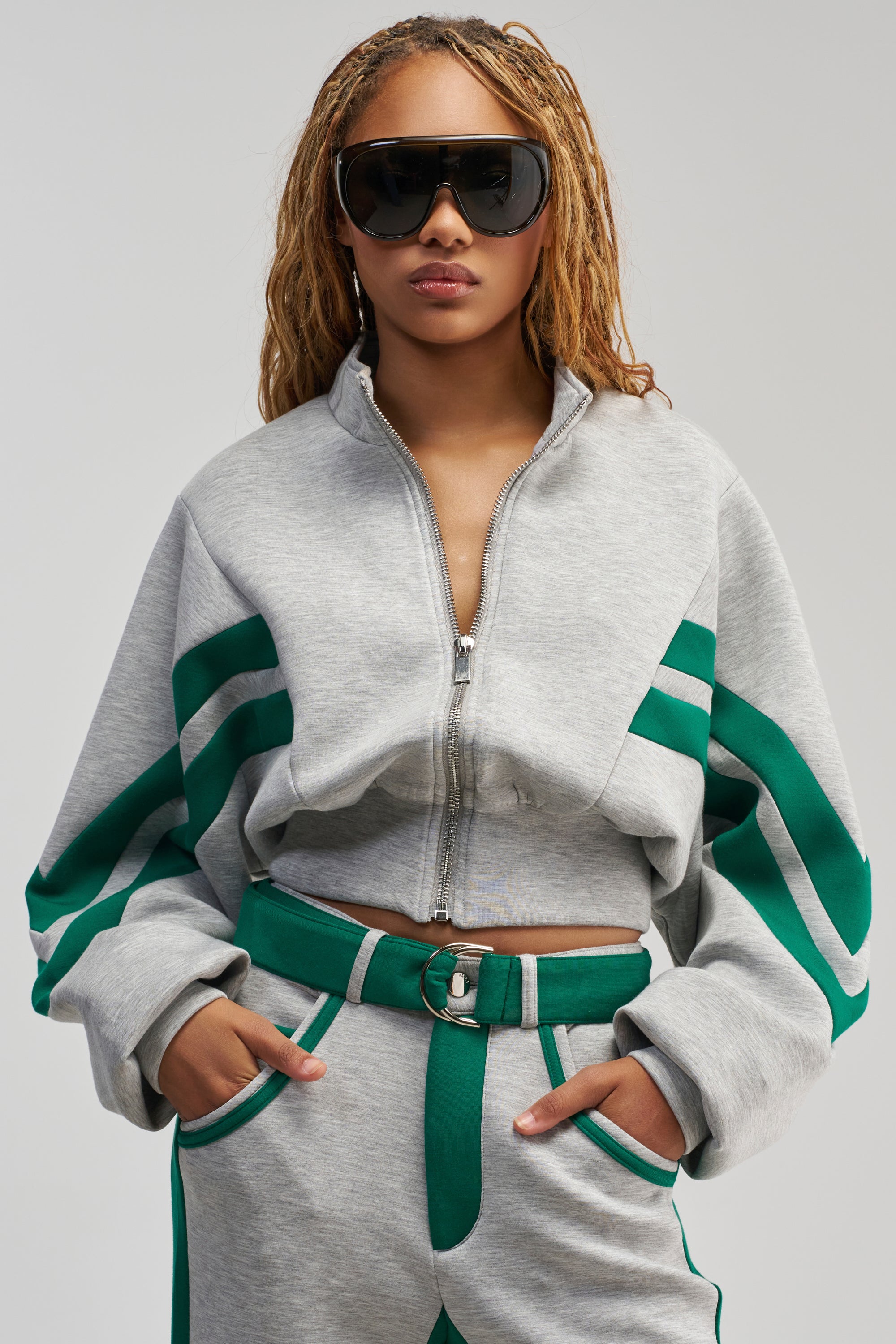 Wearing the SPORT MODE SCUBA BOMBER IN GREY, which features bold green racing stripes and oversized sunglasses, a person stands confidently with hands in pockets against a plain background, exuding effortlessly cool streetwear vibes.