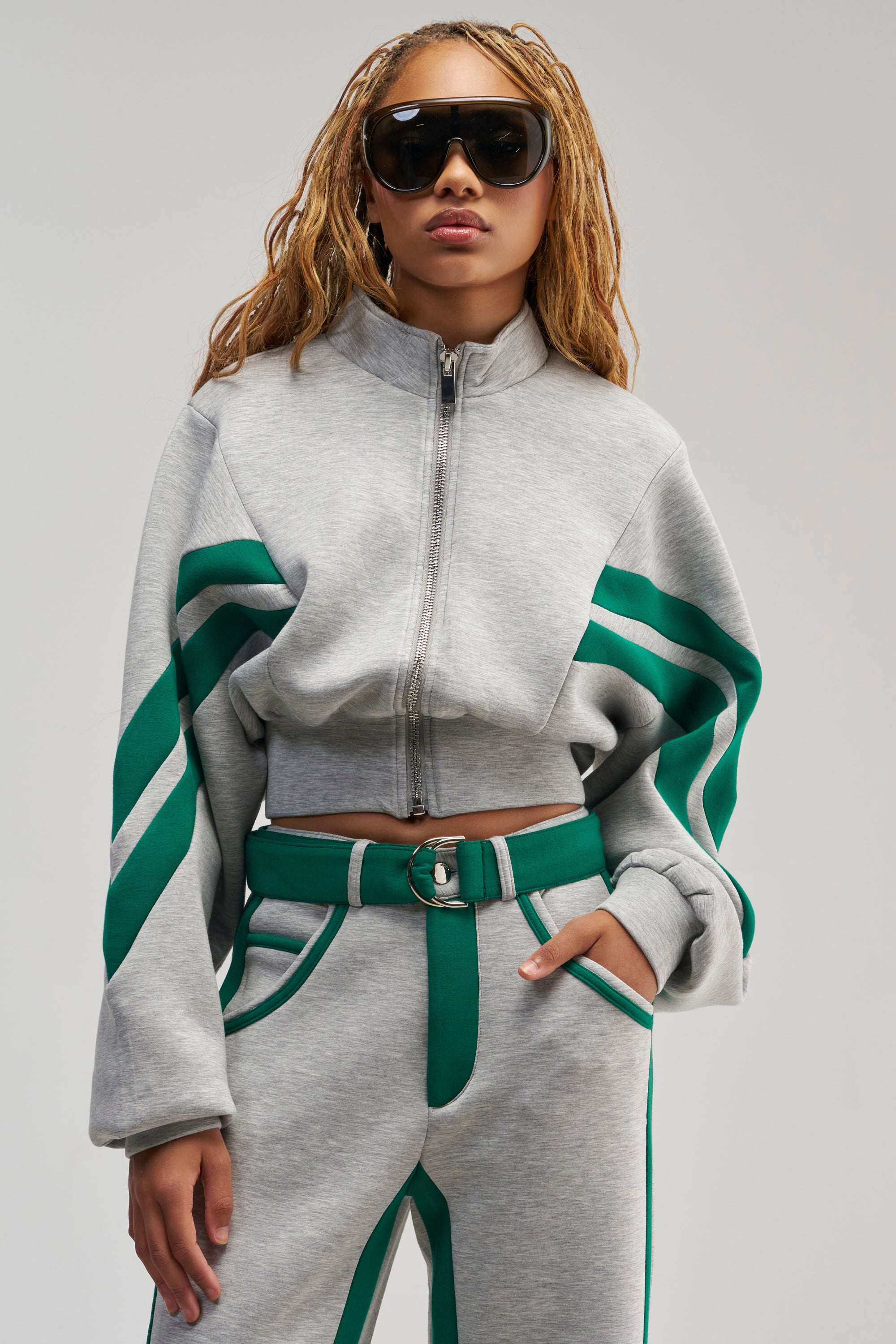 Wearing the SPORT MODE SCUBA BOMBER IN GREY, paired with matching pants and bold green racing stripes, a person with long braided hair and large black sunglasses poses confidently against a neutral background, embodying effortlessly cool streetwear style.
