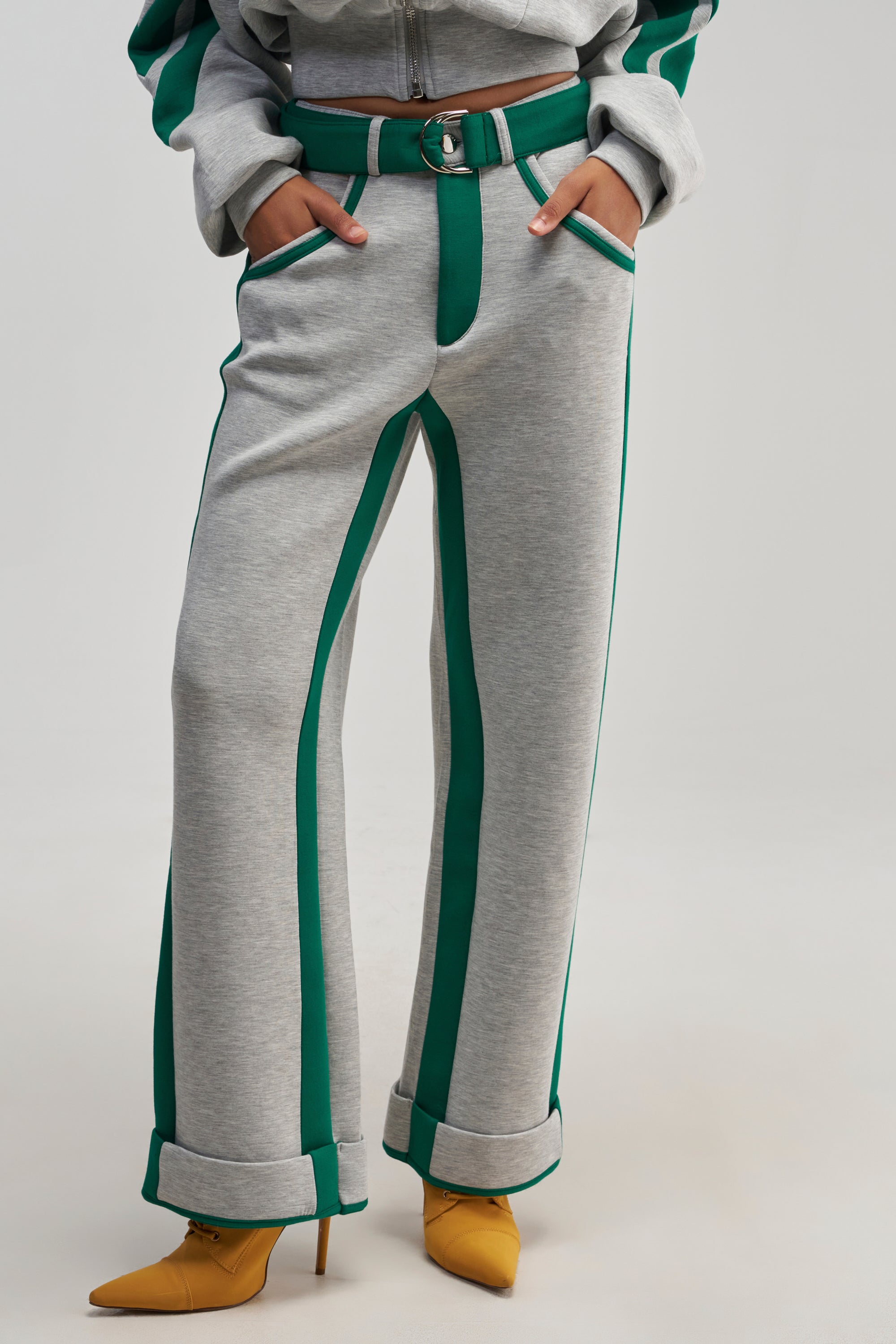 Wearing the SPORT MODE SCUBA PANT IN GREY, which features green racing stripes down the sides, a matching belt, and pockets. The outfit is paired with mustard yellow pointed-toe heeled shoes, with only the upper body partially visible.