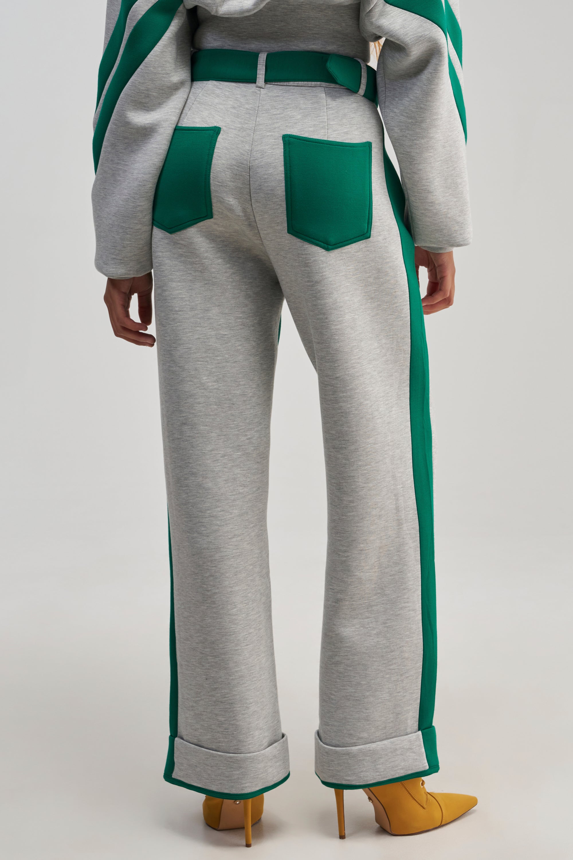 A person is shown from the back against a plain background wearing the SPORT MODE SCUBA PANT IN GREY, featuring green racing stripes along the sides and back pockets, paired with a matching gray and green streetwear-inspired top and yellow pointed-toe heels.