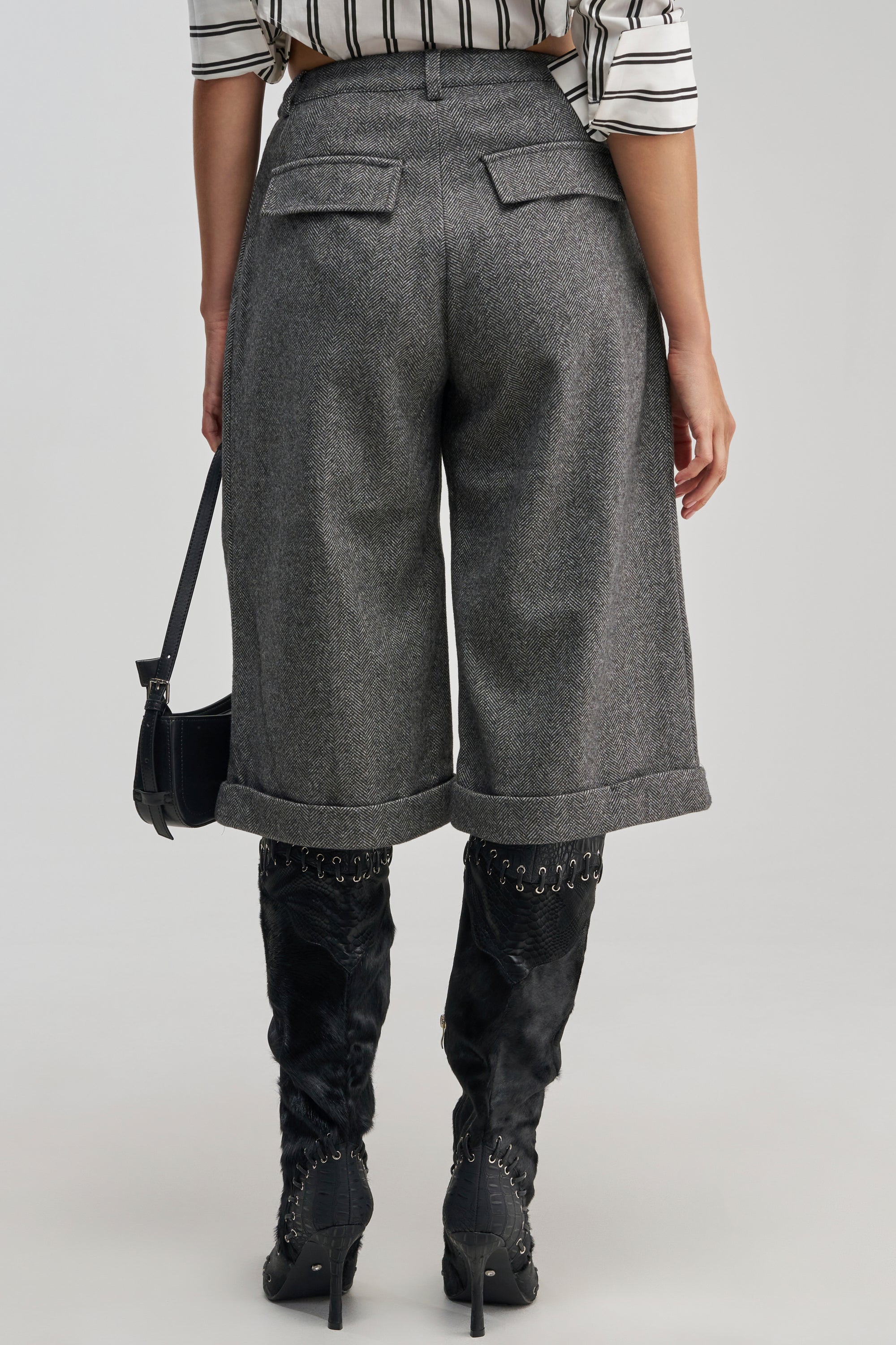 Wearing the SIREN HIGH RISE TROUSER in stylish grey tweed, a person seen from behind pairs them with a black and white striped top, black lace-up boots, and carries a small black handbag.