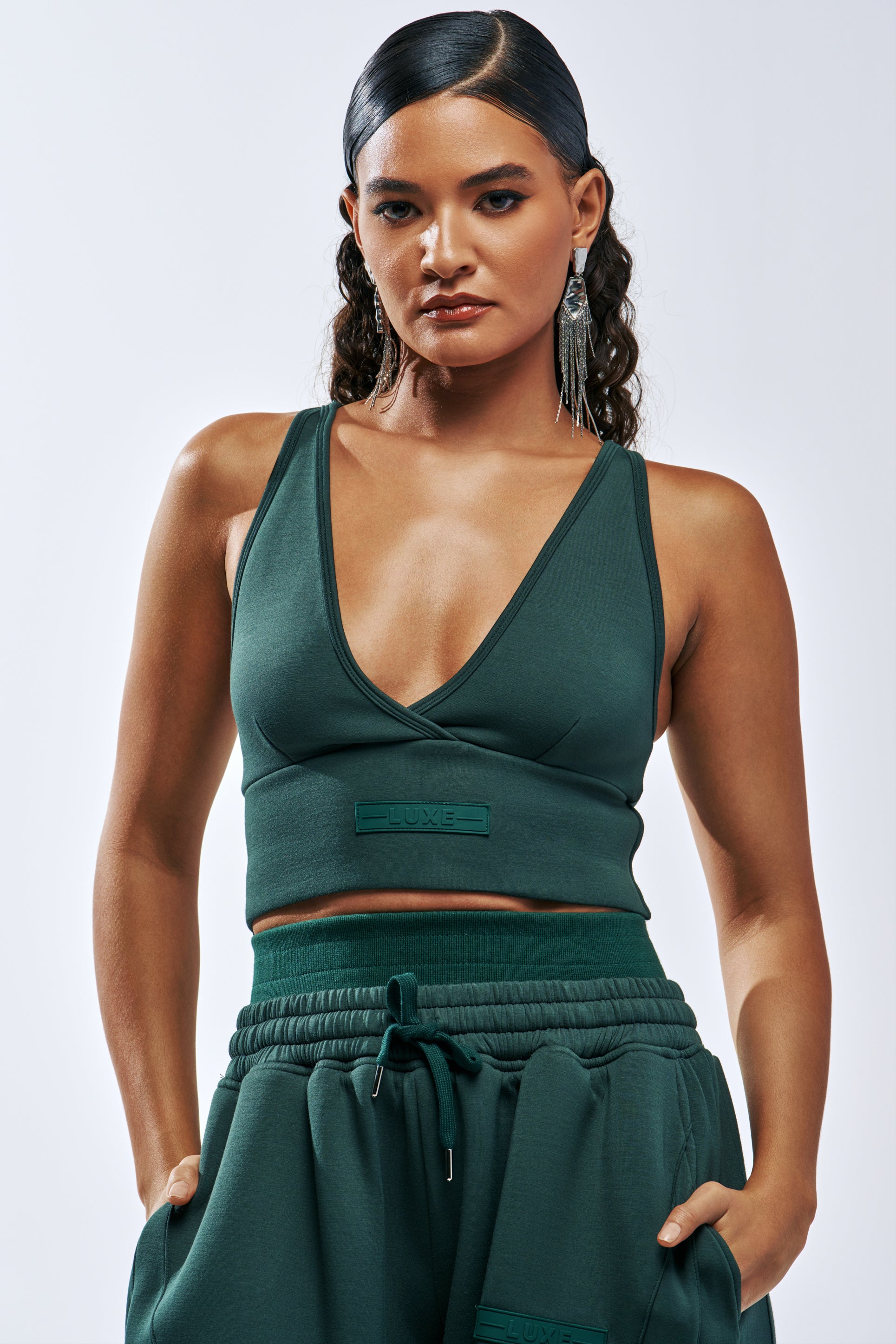 A person wearing a dark green PAXTON LUXE EVERYDAY ICON BRALETTE with a deep V-neck and matching sweatpants in an elevated loungewear set.