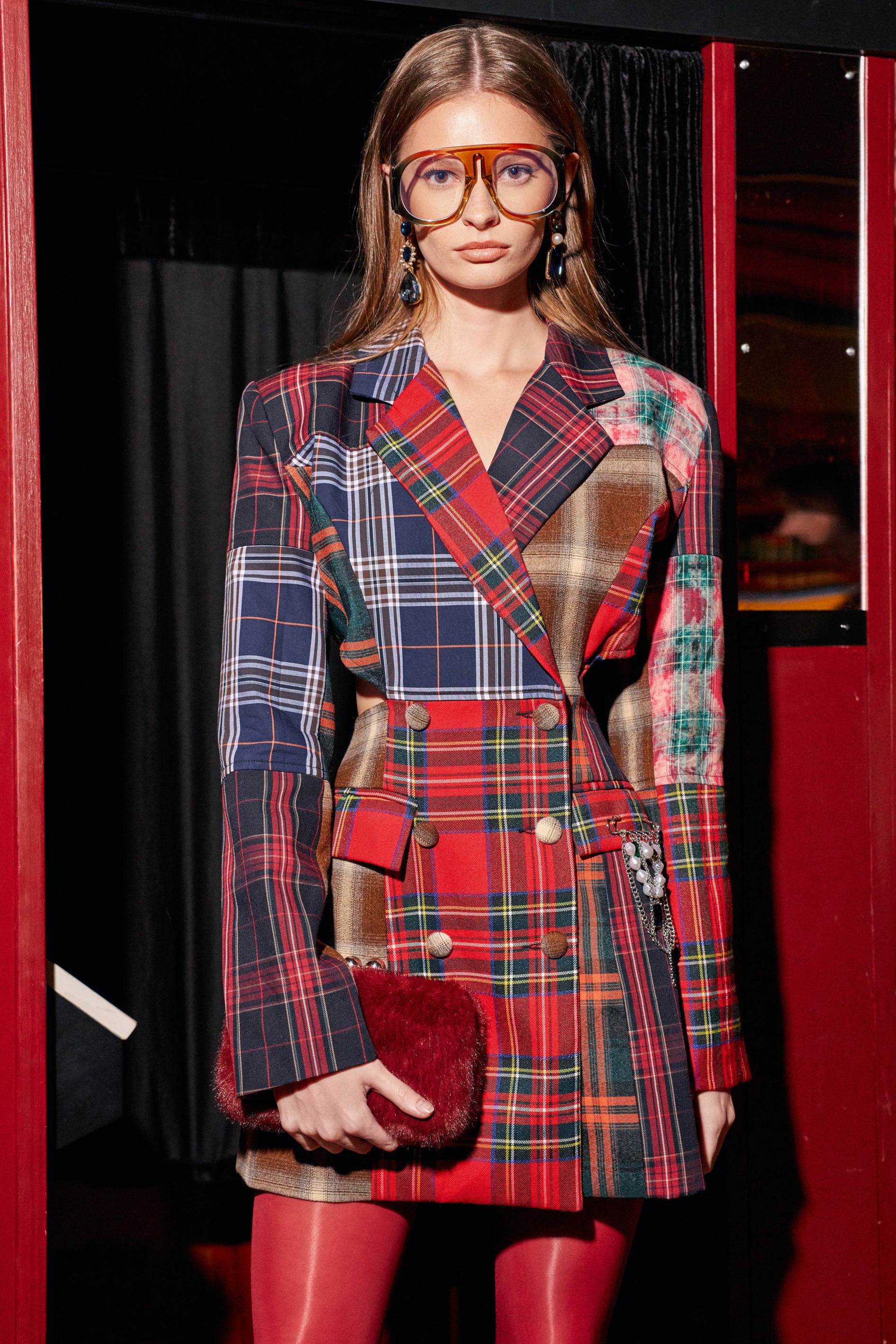 A person wears an OFFICE MUSE CUTOUT PLAID MINI DRESS featuring mismatched patterns and side cutouts, styled with oversized glasses and a red fuzzy clutch for an edgy fall outfit.
