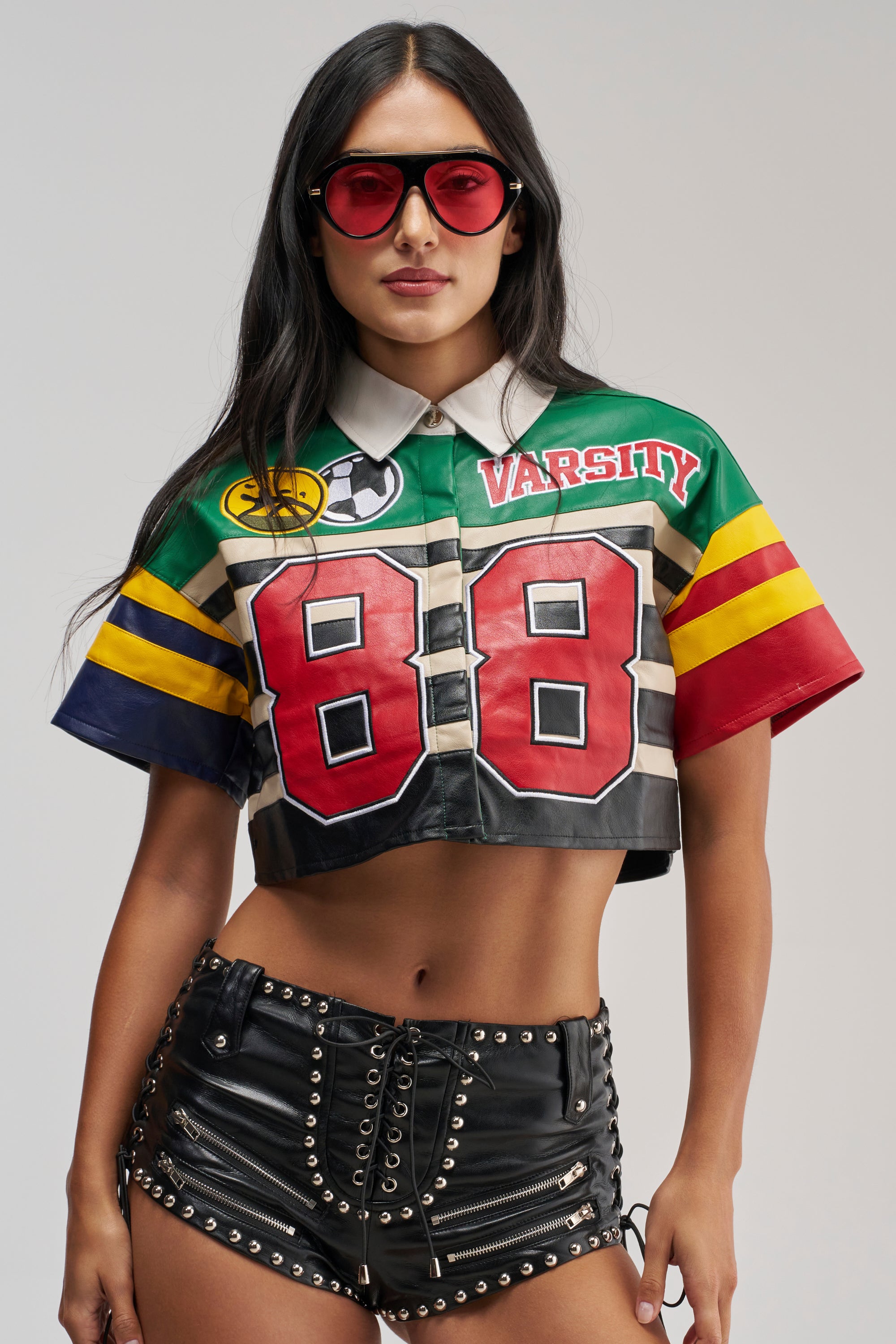 A woman stands against a plain background wearing red sunglasses and the BACK TO SCHOOL VIBES PU BUTTON DOWN, styled with black streetwear-inspired lace-up leather shorts.