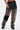 Wearing the STEPHANIA TRANSPARENT TROUSER IN BLACK, featuring a wide leg, sheer black fabric, and a large pocket on one leg. The look reveals skin and tattoos beneath, with the midriff and one arm partially visible. Styled with chunky boots.