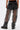 A person stands facing away, wearing AKIRA Label’s STEPHANIA TRANSPARENT TROUSER IN BLACK—see-through mesh pants over black shorts with two buttoned back pockets, styled with black boots.