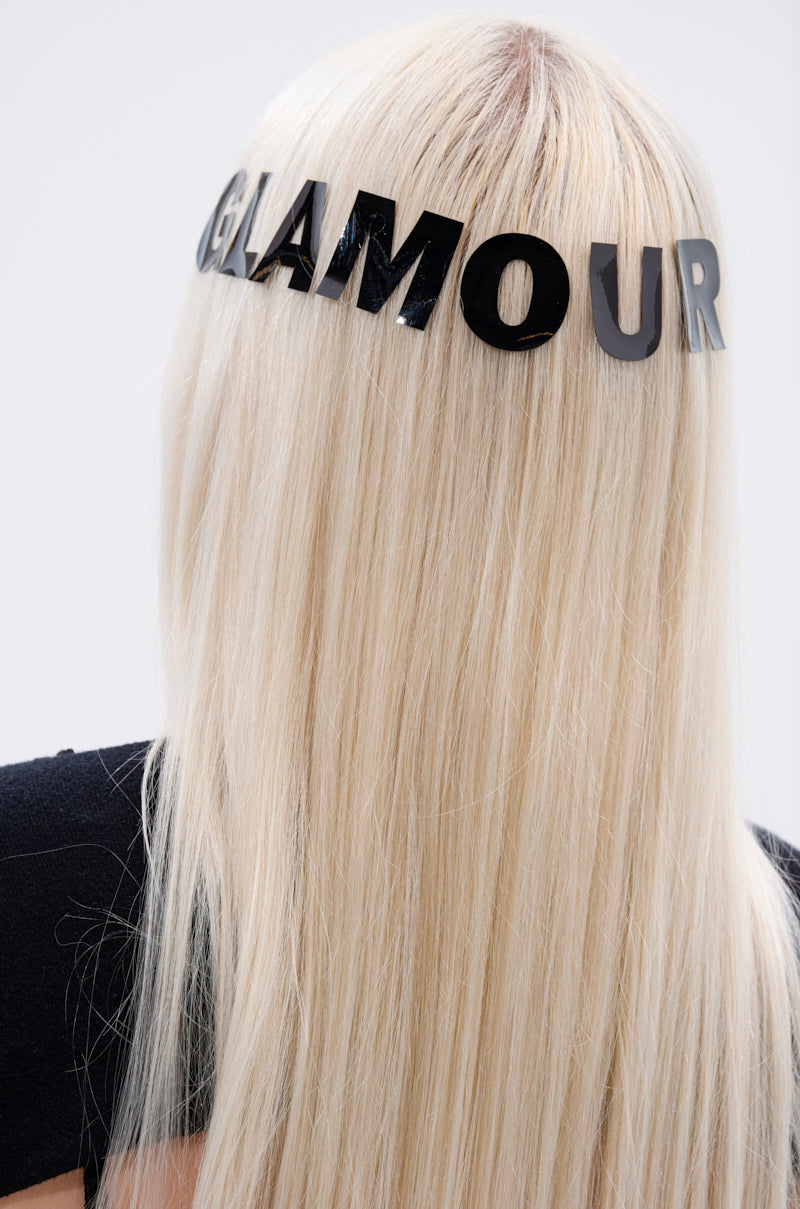 A person with long, straight platinum blonde hair is seen from behind, wearing a black headband with "GLAMOUR" in bold letters and the GLAMOUR BODY AND HAIR STICKER as a sparkling accent. 1