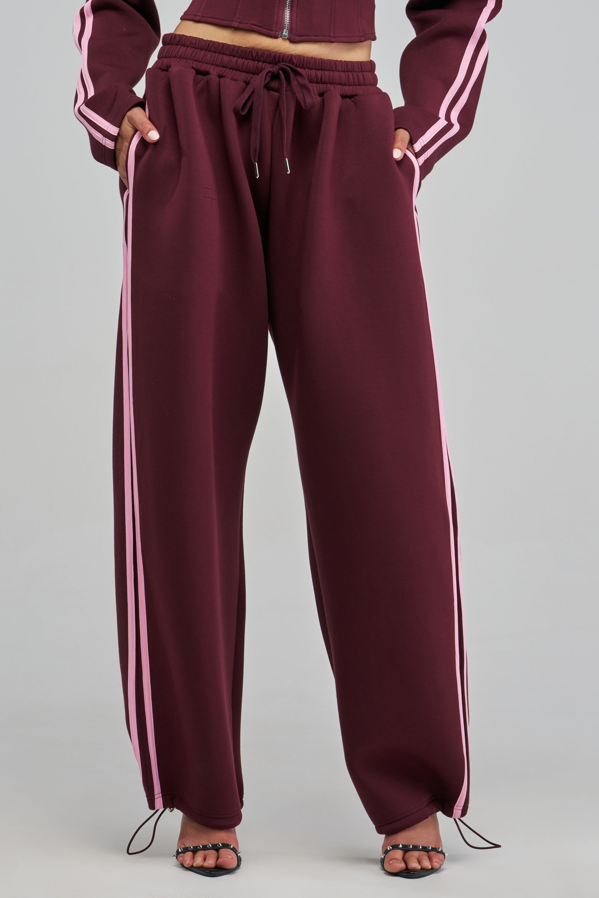 PAXTON LUXE STRIPED JOGGER track pants in maroon with pink side stripes and a drawstring waist, worn with a matching zip-up jacket for a sporty fall look.