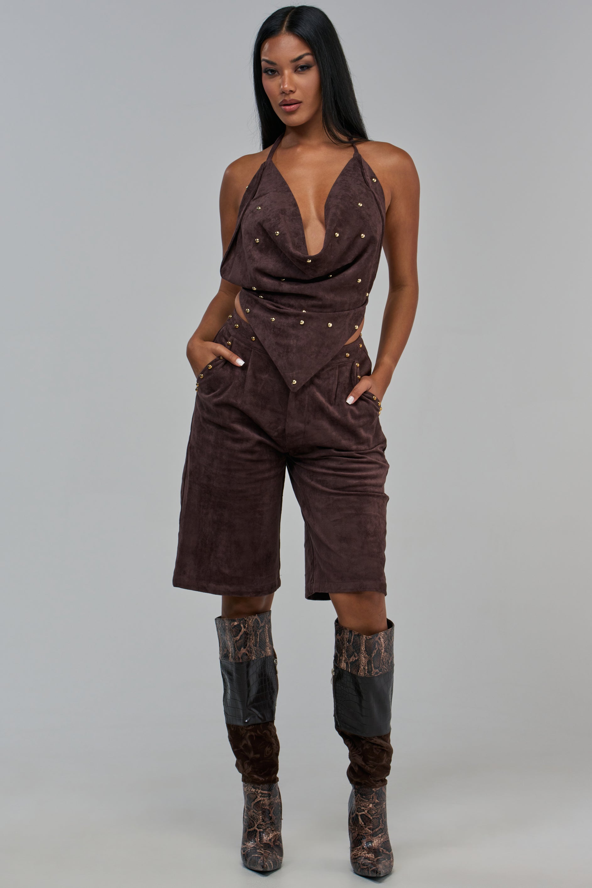 A woman wears a brown faux suede halter top with gold studs and GIA SUEDE PANT knee-length culottes, paired with knee-high snakeskin-patterned boots.