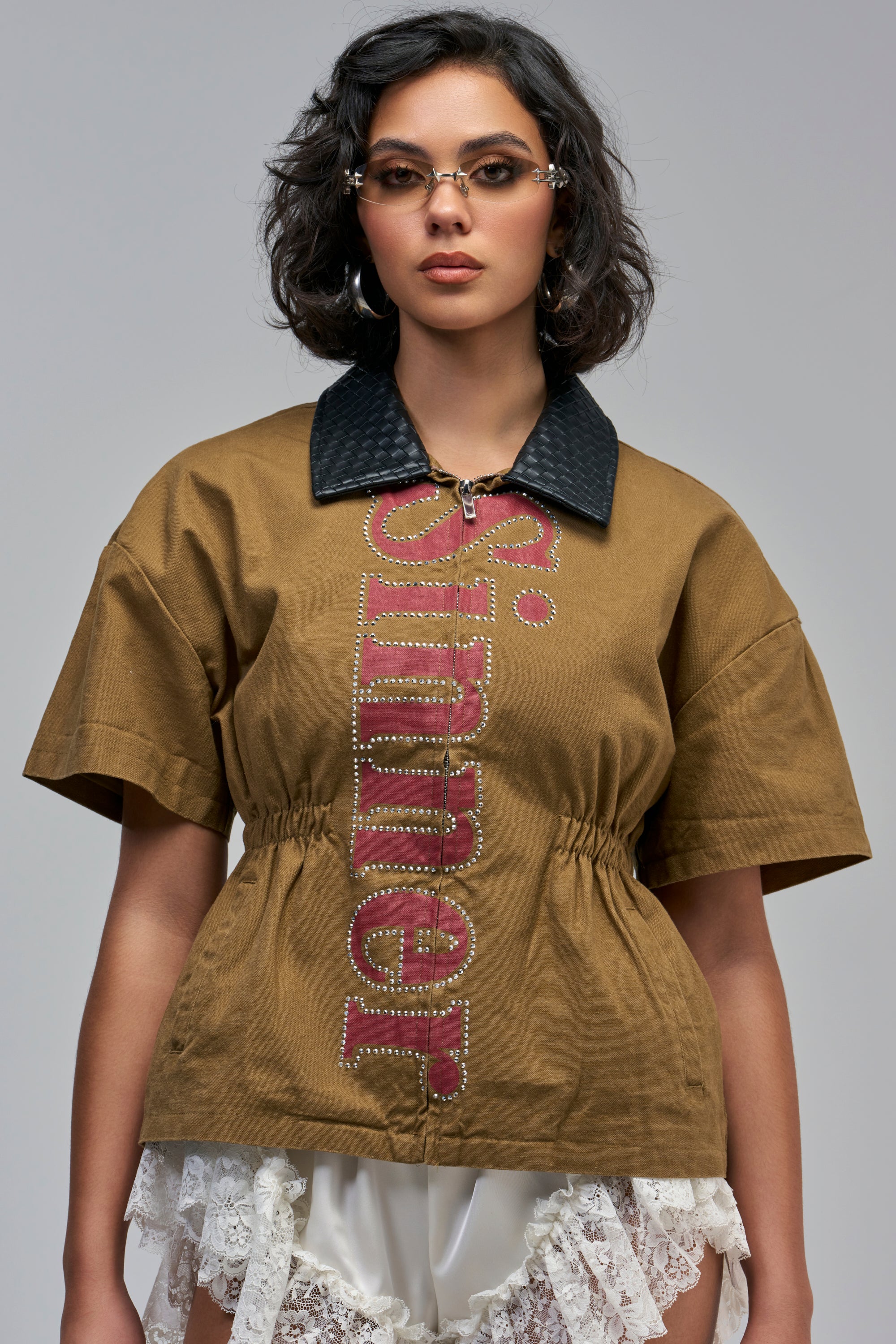 STATEMENT CINCH SHORT SLEEVE TOP in brown with a black collar, a vertical “Sinner” graphic in red with rhinestone detailing, and a cinched waist.