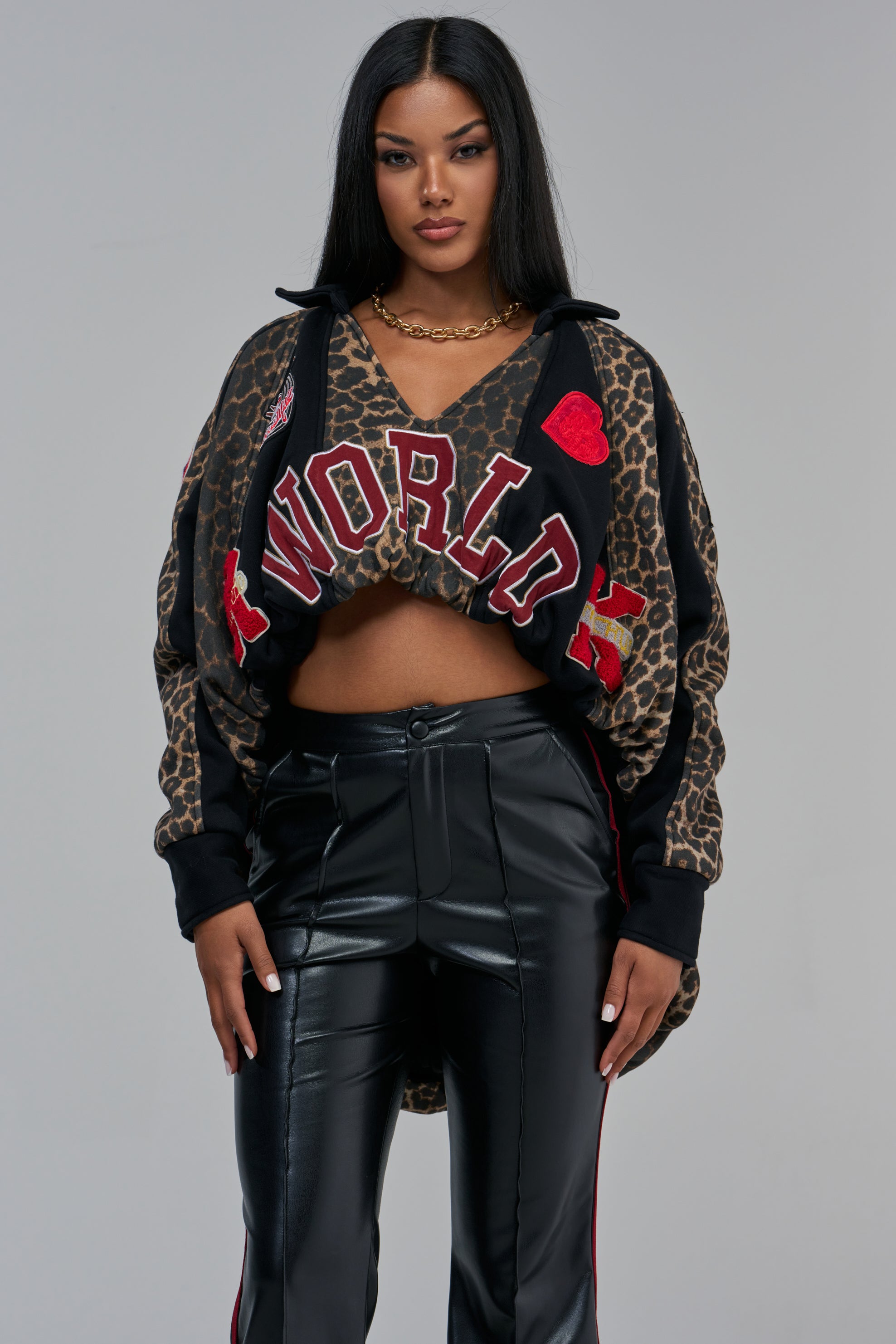 A DREAM GIRL PATCHWORK HIGH LOW SWEATSHIRT, shown as a cropped leopard print sweatshirt with varsity patch “WORLD” graphic sleeves worn with black pants.