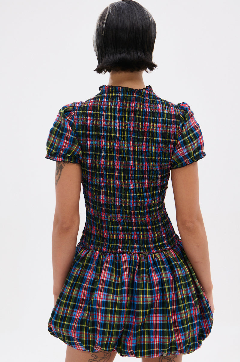 A person with short dark hair, seen from behind, wears the THAT GIRL PLAID MINI DRESS featuring puff sleeves, a smocked bodice, and a flared bubble skirt.