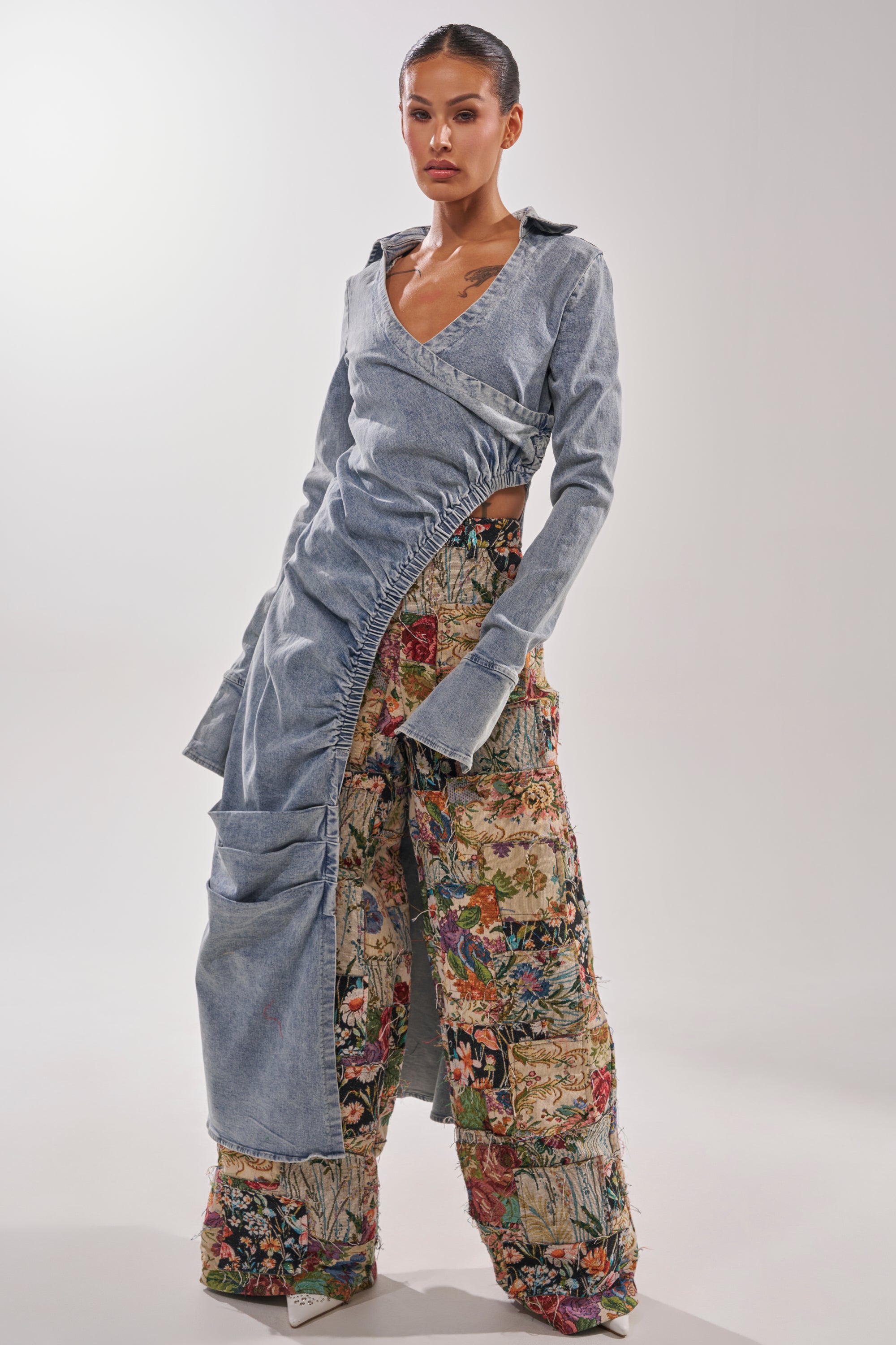 A woman wears the GET MY CLOSE UP EMBELLISHED BUTTON DOWN SHIRT, styled with wide, quilted patchwork pants featuring colorful floral patterns. The modern look is set against a plain, well-lit background. 1