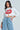 Wearing the bold LIPS BUTTON DOWN TOP, a person confidently stands with long, wavy hair. Their high-waisted blue jeans feature decorative holes that complement the eye-catching top. The plain, well-lit background highlights their fashionable style.