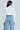 A person with long dark hair wears the LIPS BUTTON DOWN TOP, a white cropped button-up made from poplin, paired with high-waisted wide-leg blue jeans decorated with small white pearls. They stand facing away from the camera against a plain background.