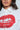 Someone is wearing a stylish LIPS BUTTON DOWN TOP with a bold glittery red lip graphic. The elegant poplin fabric highlights intricate detailing, as the face is partially visible.