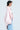 A person stands in profile against a white background, wearing the oversized FIRST CLASS COCOON COAT in light pink padded satin, along with a white tube top and blue jeans. They have short dark hair and are accessorized with large, intricate earrings.