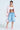 A person in the oversized FIRST CLASS COCOON COAT in pink combines it with a white bandeau, distressed denim shorts, and pink furry slippers. They accessorize with statement jewelry and carry a padded satin shoulder bag. Tattoos adorn their midriff against a light gray backdrop.