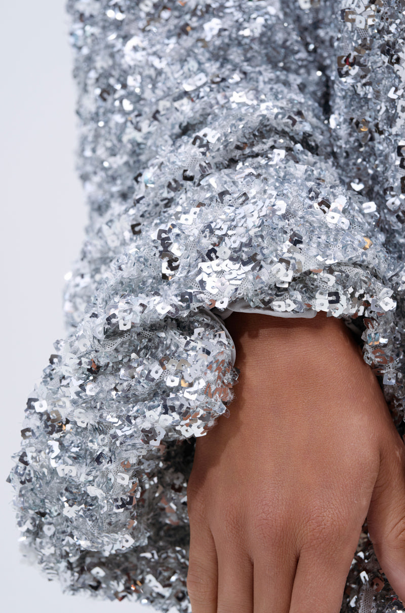A close-up of a hand partly covered by the GISELLE SEQUIN SWEATSHIRT DRESS IN SILVER, featuring sparkling silver sequins for a textured effect.
