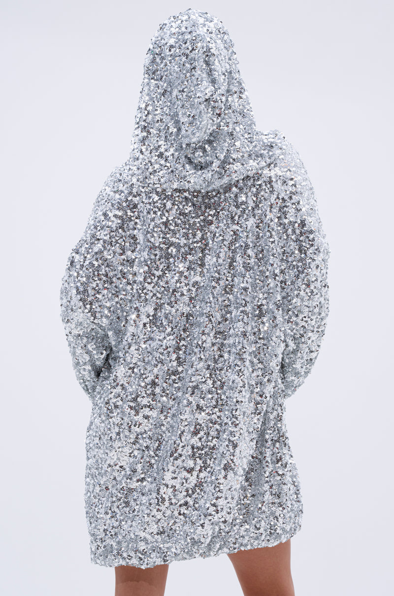 A person faces away from the camera, showcasing the back and legs below the hem of the GISELLE SEQUIN SWEATSHIRT DRESS IN SILVER against a plain light background.