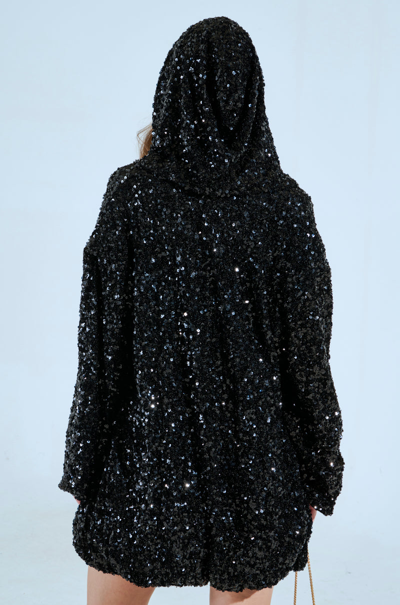 Wearing the GISELLE SEQUIN SWEATSHIRT DRESS, a person faces away against a light background, arms by their sides as its black sequined embellishments sparkle. 4