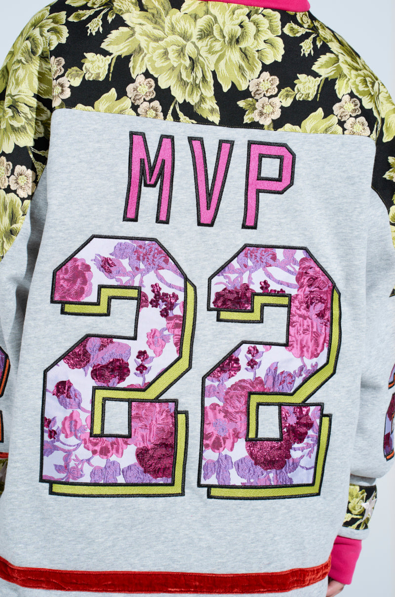 The ATHLETIC BROCADE SWEATSHIRT DRESS showcases a bold oversized silhouette with "MVP" and "22" on the back, adorned with floral designs. The top features a green floral brocade pattern on black, contrasting with a light gray base.