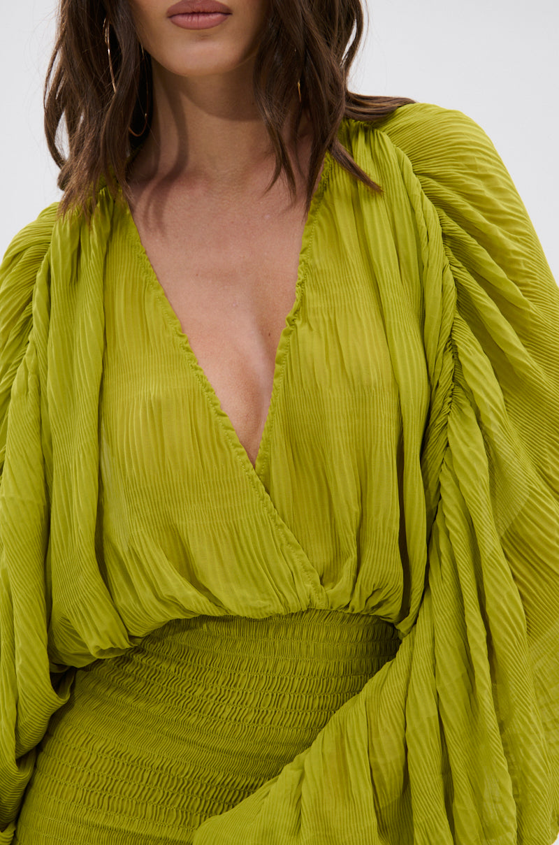 A woman in the NIGHTS LIKE THIS CHIFFON MINI DRESS, a vibrant pleated chartreuse style with a deep V-neck and billowy long sleeves. Her loose, wavy hair partially hides her face. 8