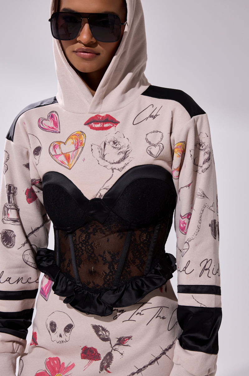 Wearing the SNATCH ME UP CORSET SWEATSHIRT DRESS—an oversized hoodie dress with hearts, lips, flowers, and handwritten text in black and pink doodles—layered under a lace corset overlay and styled with dark sunglasses against a plain background.