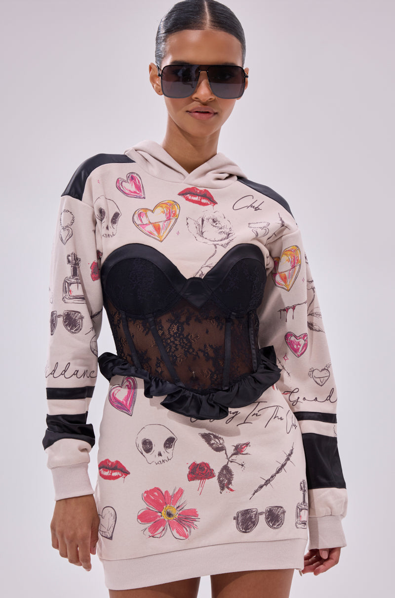 A woman wears the SNATCH ME UP CORSET SWEATSHIRT DRESS, an oversized hoodie dress with colorful sketches and a black floral lace corset layered over it, paired with large dark sunglasses.