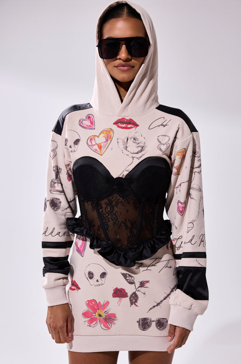 A woman confidently poses against a plain background in the SNATCH ME UP CORSET SWEATSHIRT DRESS, featuring oversized doodle prints and a black lace corset detail, paired with large black sunglasses.