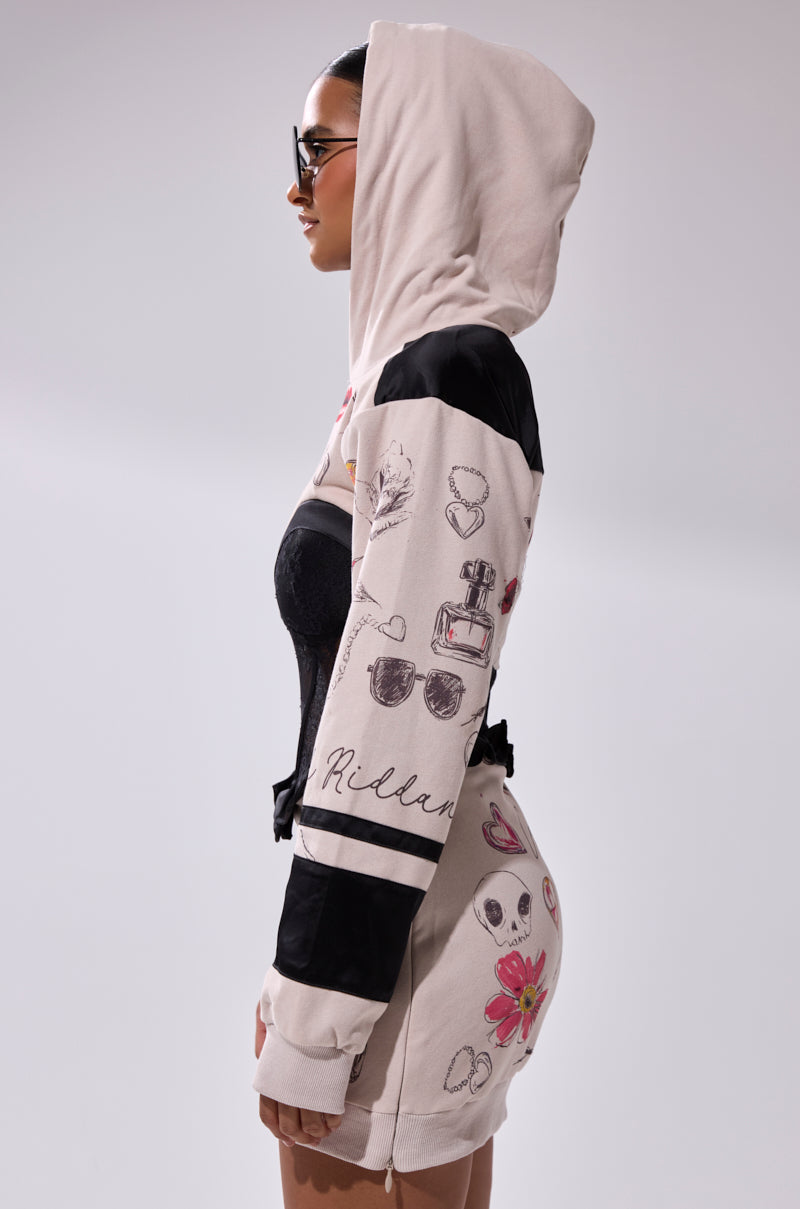 A woman in profile models the SNATCH ME UP CORSET SWEATSHIRT DRESS, featuring black accents and graphic prints like sunglasses, perfume, flowers, and hearts. She pairs it with sunglasses and styles a lace corset under the dress.