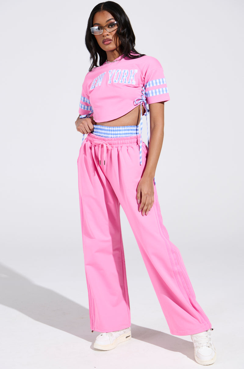 A person in a pink NEW YORK GINGHAM CROP TOP paired with matching pants, accessorized with sunglasses and white sneakers, standing confidently against a plain background.