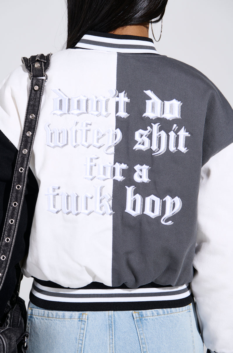 The image depicts a person from behind wearing a NOT YOUR BABE EMBROIDERED BOMBER with bold text, "don't do wifey shit for a fuck boy," on the back. They have long hair, light blue jeans, and carry a black bag.