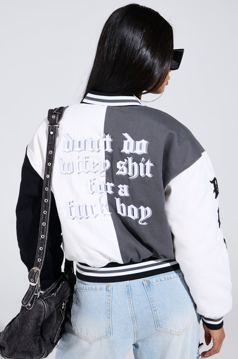 Wearing the NOT YOUR BABE EMBROIDERED BOMBER and light blue jeans, person sports long dark hair, sunglasses, and a black handbag. The bold text on the jacket adds an edgy vibe against a plain background.