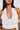 A woman with long dark hair, gold hoop earrings, and light brown lipstick models the TIED TO YOU FRINGE TANK—a sheer white lace mesh crop top with ruffle and textured details. The image is cropped below her shoulders.
