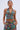 A woman wears the LOGAN JACQUARD LACE UP CORSET TOP, featuring a vibrant floral pattern and lace-up detailing, paired with matching pants. She stands with her hands in her pockets against a plain light background.