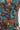 A close-up of a person wearing the LOGAN JACQUARD LACE UP CORSET TOP, featuring lace-up details and bold, textured jacquard fabric with vibrant green, orange, purple, and yellow floral patterns.
