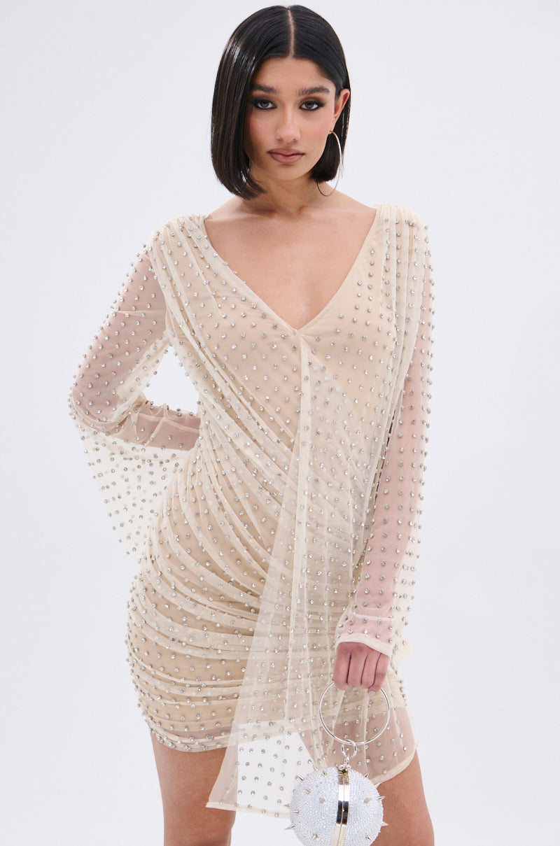 A woman with a sleek bob wears the ALYSSA RHINESTONE MINI DRESS—a nude mesh style with pearl-like embellishments. She holds a round, white beaded handbag and poses against a plain white background.